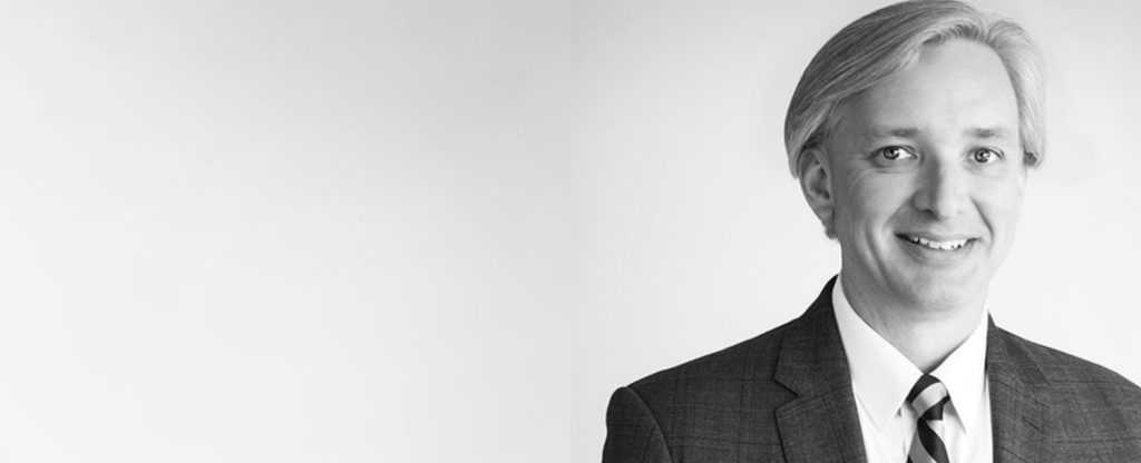Black and white headshot of Tad Bartlett, where Tad is in the right foreground and gray space extends to his left